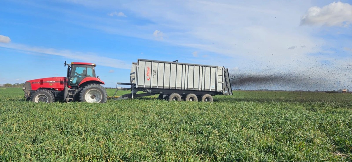 Tractor con acoplado esparcidor distribuyendo estiércol sobre un lote verde