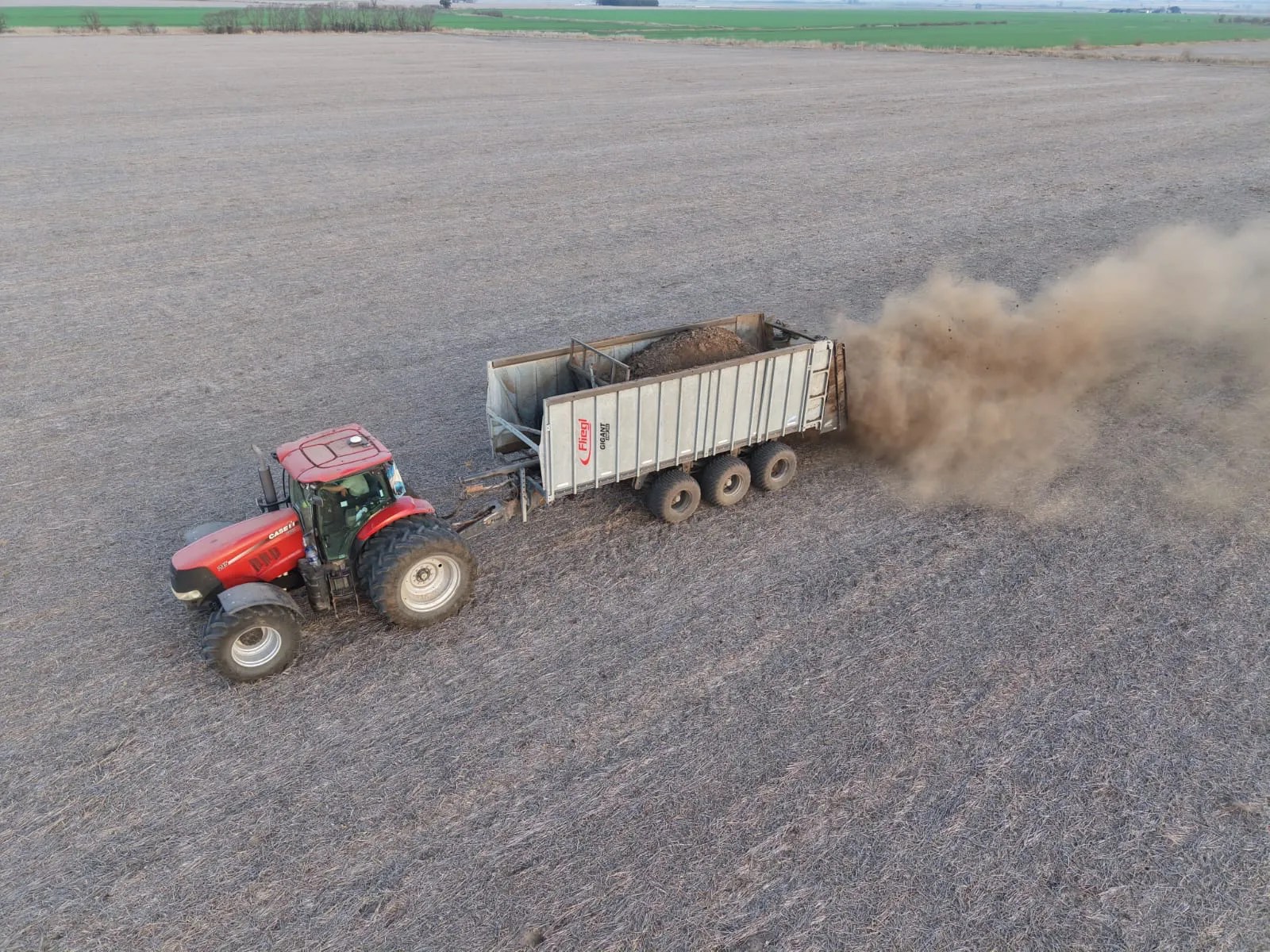 Vista aérea de un tractor con acoplado esparciendo estiércol sobre un lote